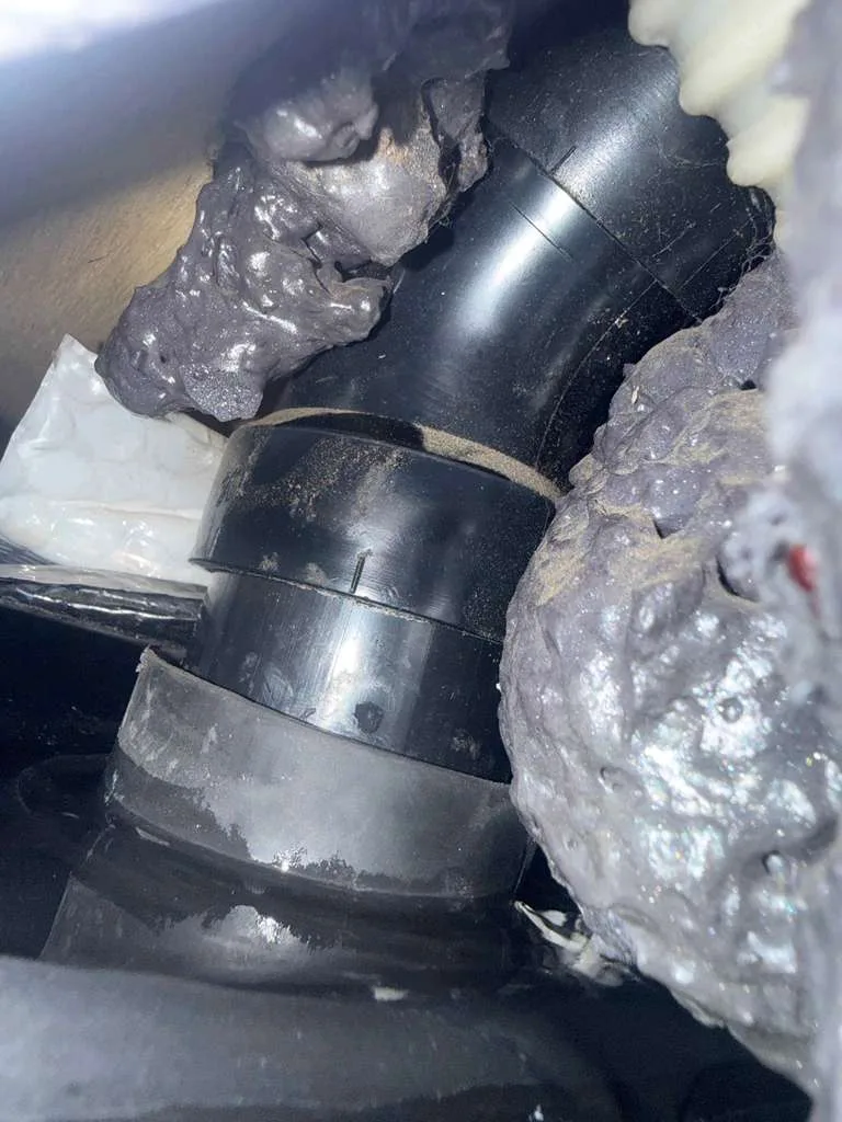 Disconnected black tank drain pipe on an RV being repaired and resealed